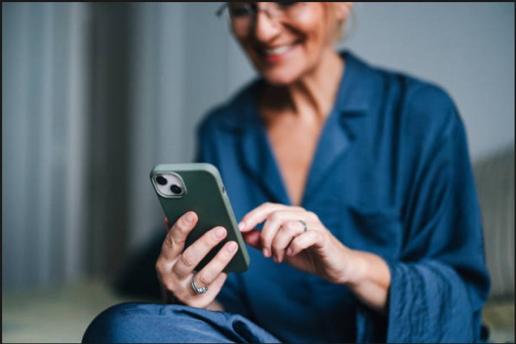 Kvinde smiler, mens hun ser sin pension på telefonen